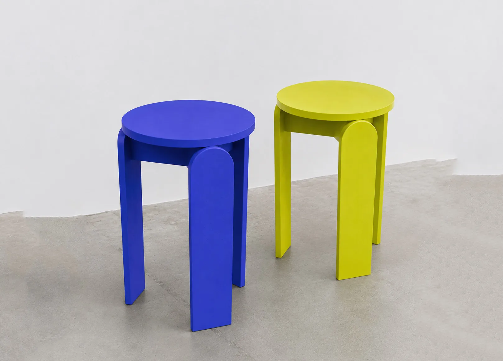Two round stools in vivid blue and yellow, each constructed from three broad curved legs and a circular seat.
