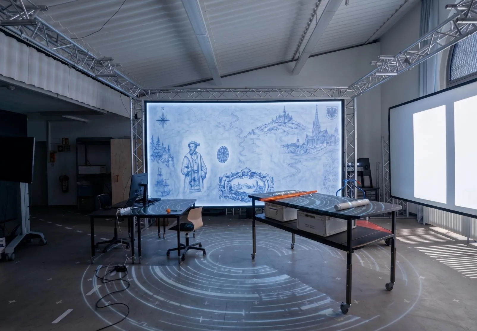 Experimental immersive lab with large wall projections, floor projection, technical equipment and movable tables.