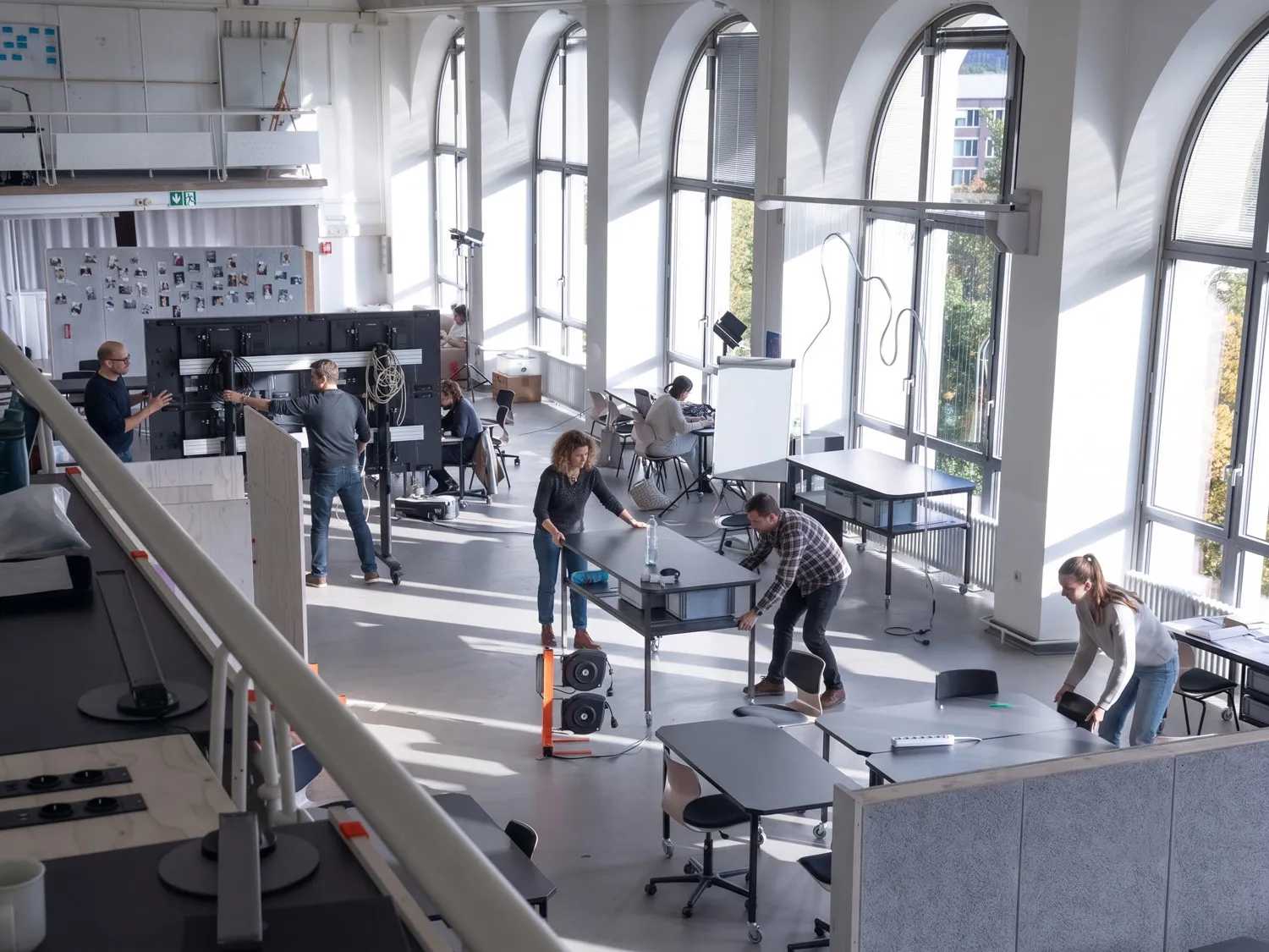 People working in the bright historic reading room while mobile tables, screens and lighting equipment are being arranged.