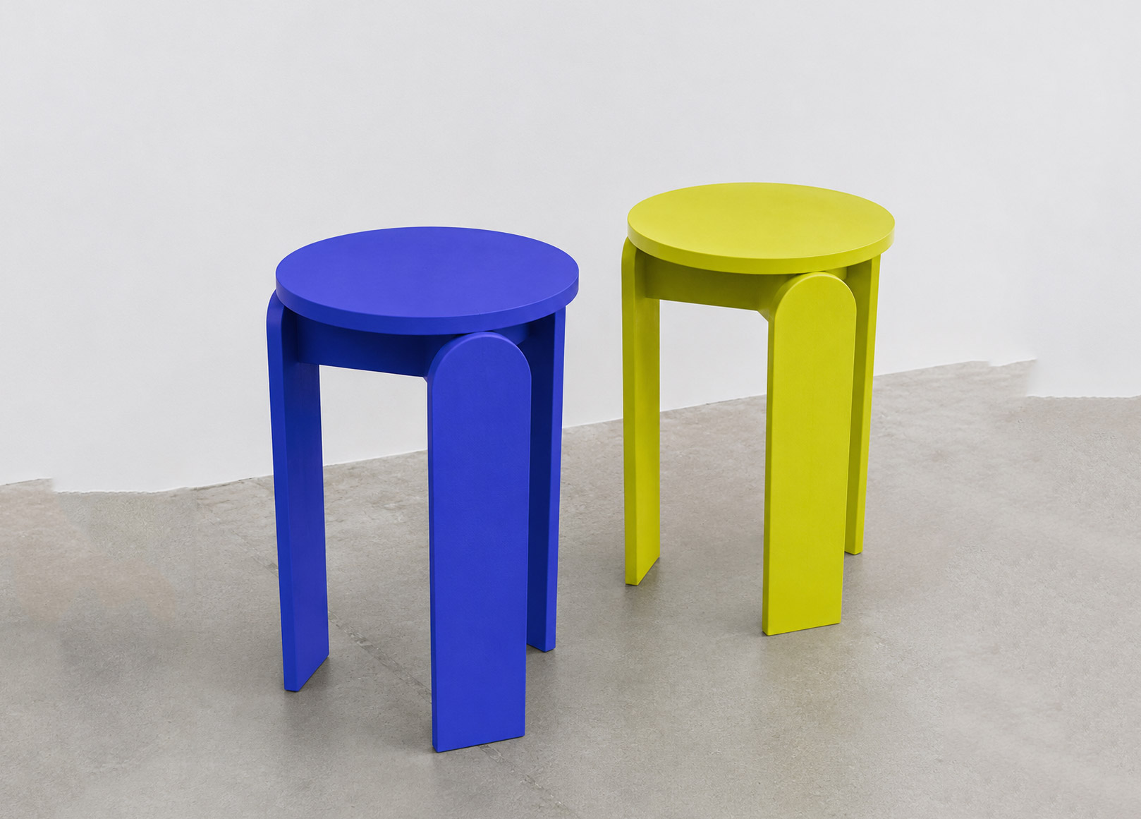 Two round stools in vivid blue and yellow, each constructed from three broad curved legs and a circular seat.